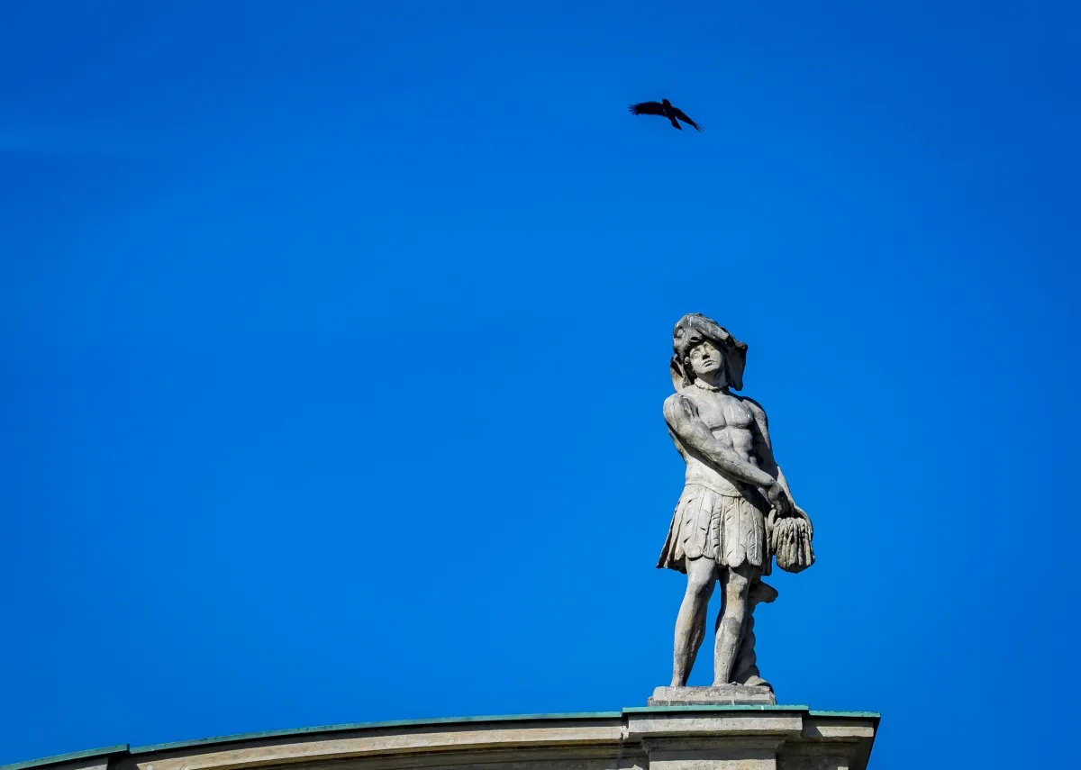 Stone rooftop statue beneath a bird crossing a deep blue sky